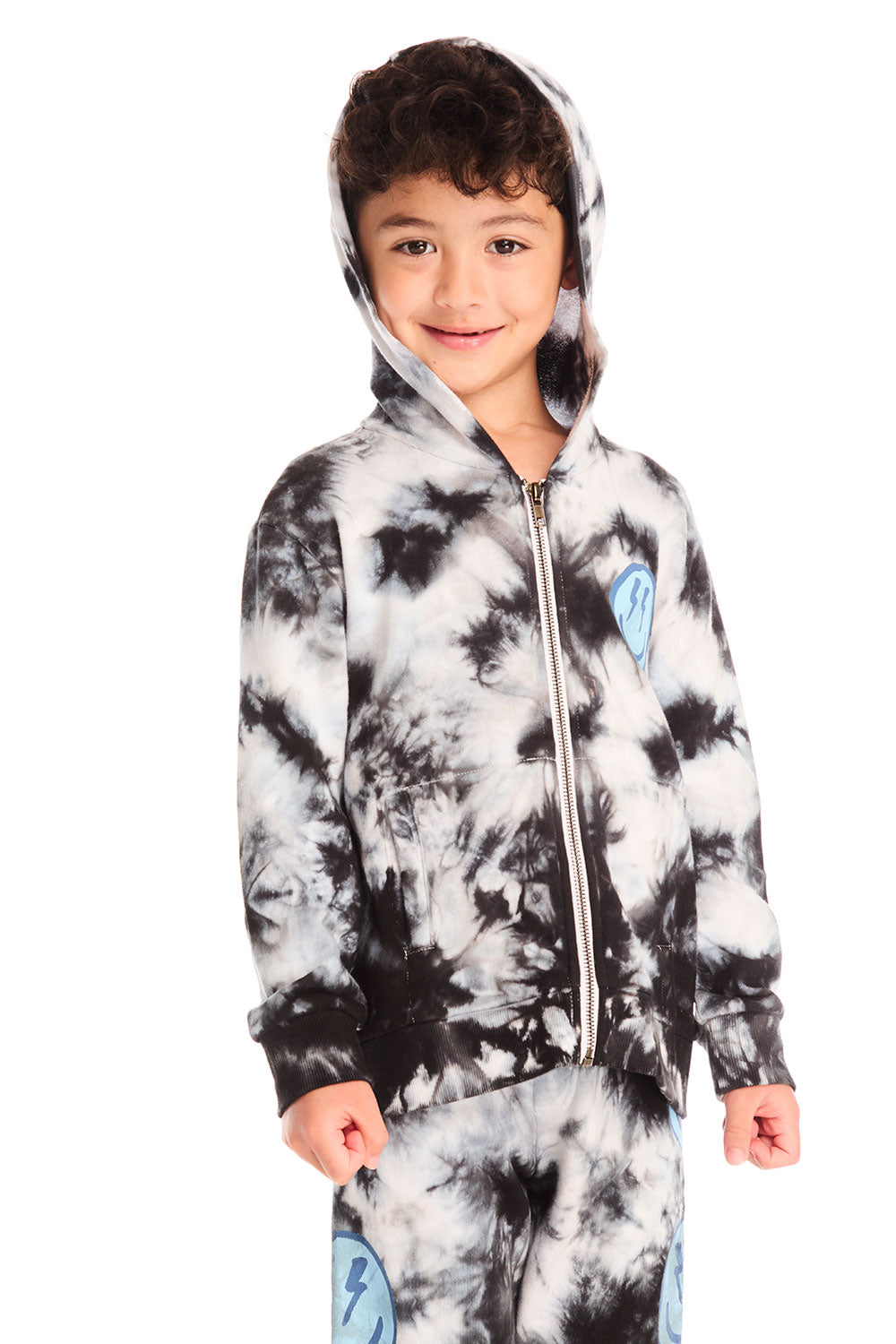 Boy wearing Chaser’s Smiley Bolt tie-dye zip up hoodie, hood up, with blue smiley face and lightning bolt eyes graphic on left chest on a white background
