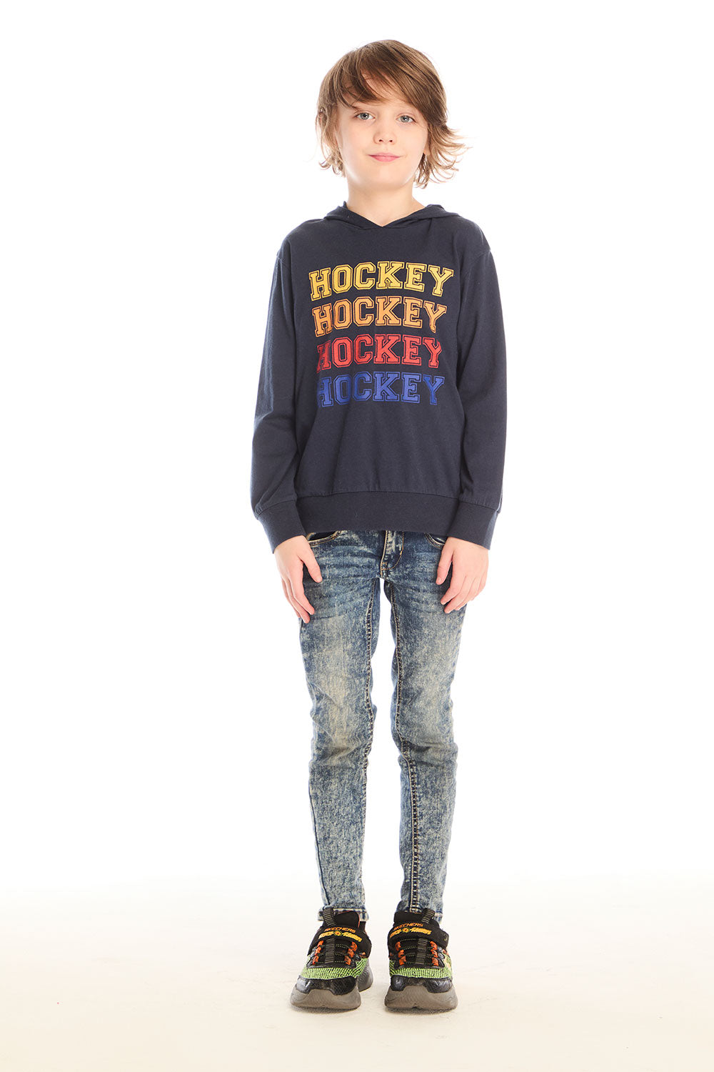 Full body view of boy wearing Chaser’s Hockey navy blue pullover hoodie with ‘Hockey’ text and distressed jeans on a white background
