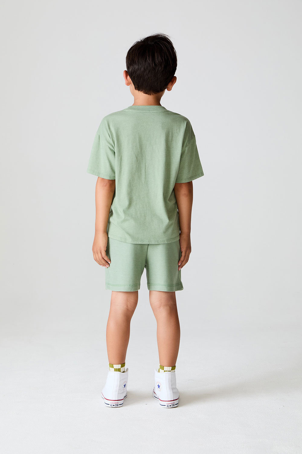 Back view of boy wearing Chaser Kids Lets go Golfing shorts and matching green t-shirt with white sneakers on a white background