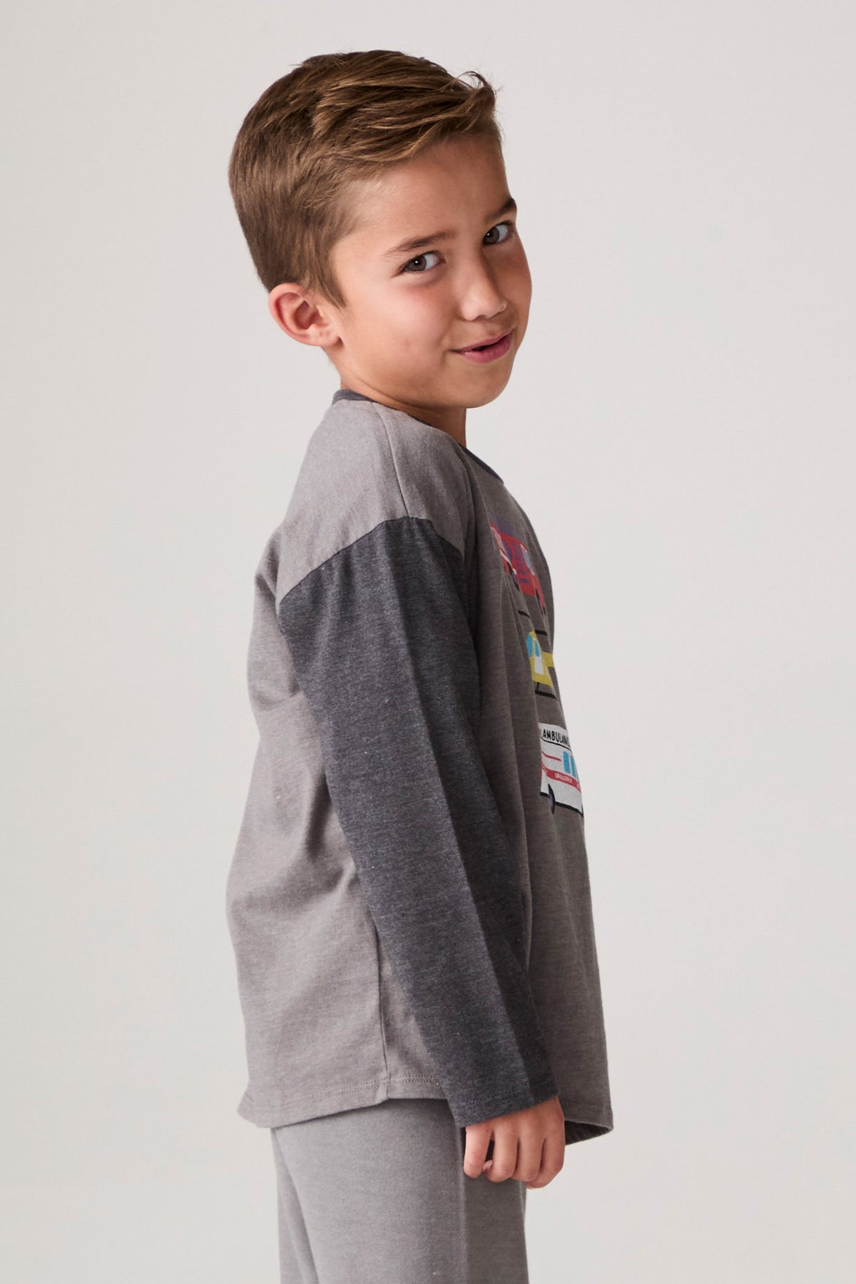 Model wearing Chaser's Heroes Boys Long Sleeve Tee in charcoal with first-responder vehicle graphics, side view