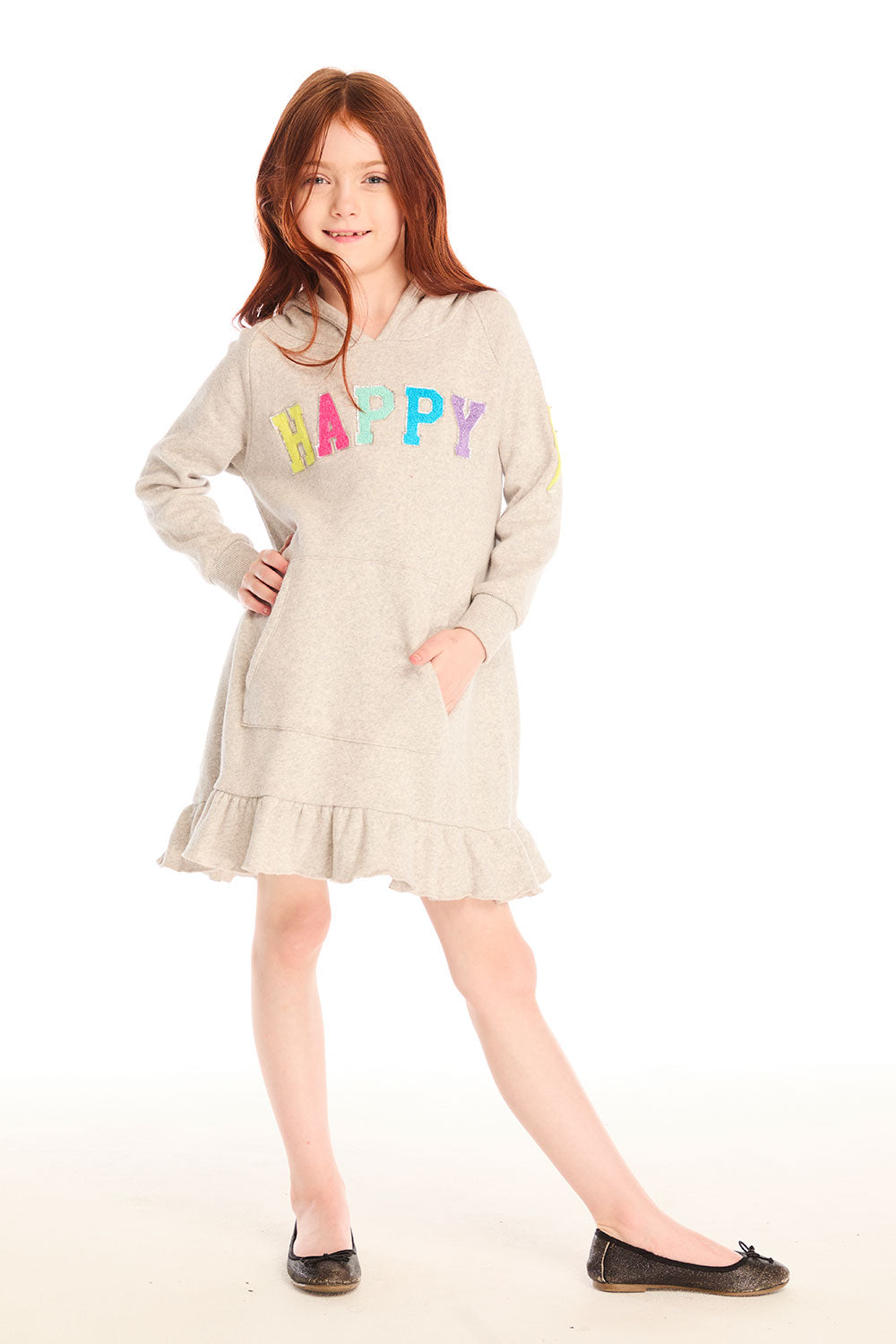 Full body view of girl wearing Chaser’s Glitter Smiley Heather Grey Hoodie Dress with long sleeves, colorful “HAPPY” letters on the front against a white background