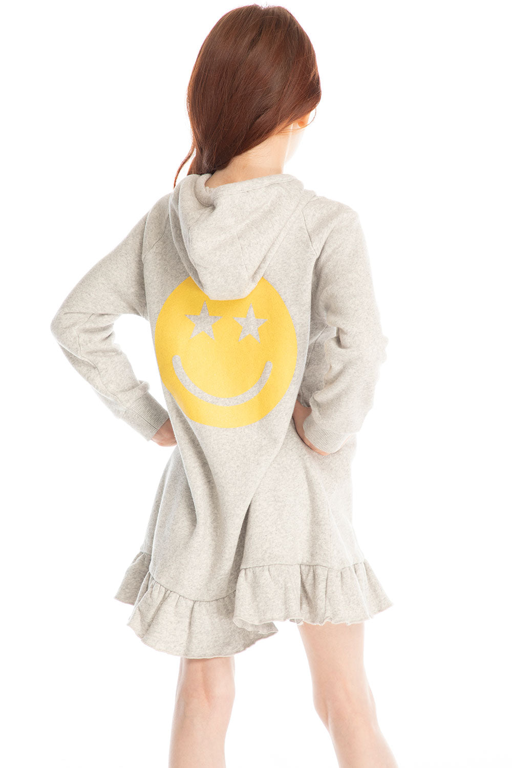 Back view of girl wearing Chaser’s Glitter Smiley Heather Grey Hoodie Dress with long sleeves and a large yellow smiley face graphic on the back against a white background