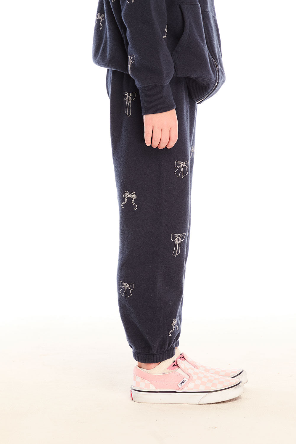 Side view of girl wearing Chaser’s navy blue Tossed Glitter Bows Pants with embroidered bows on a white background