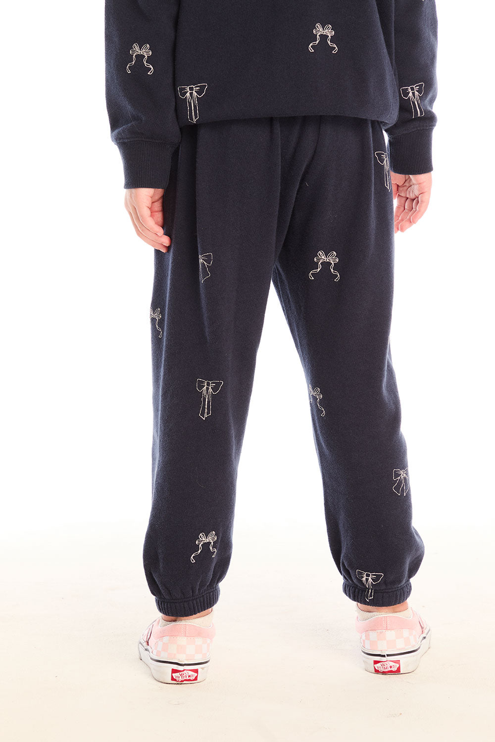 Back view of girl wearing Chaser’s navy blue Tossed Glitter Bows Pants with embroidered bows on a white background