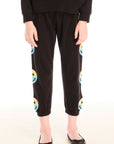 Girl wearing Chaser’s black Pastel Rainbow Smiley Pants with pastel-colored smiley face designs on a white background