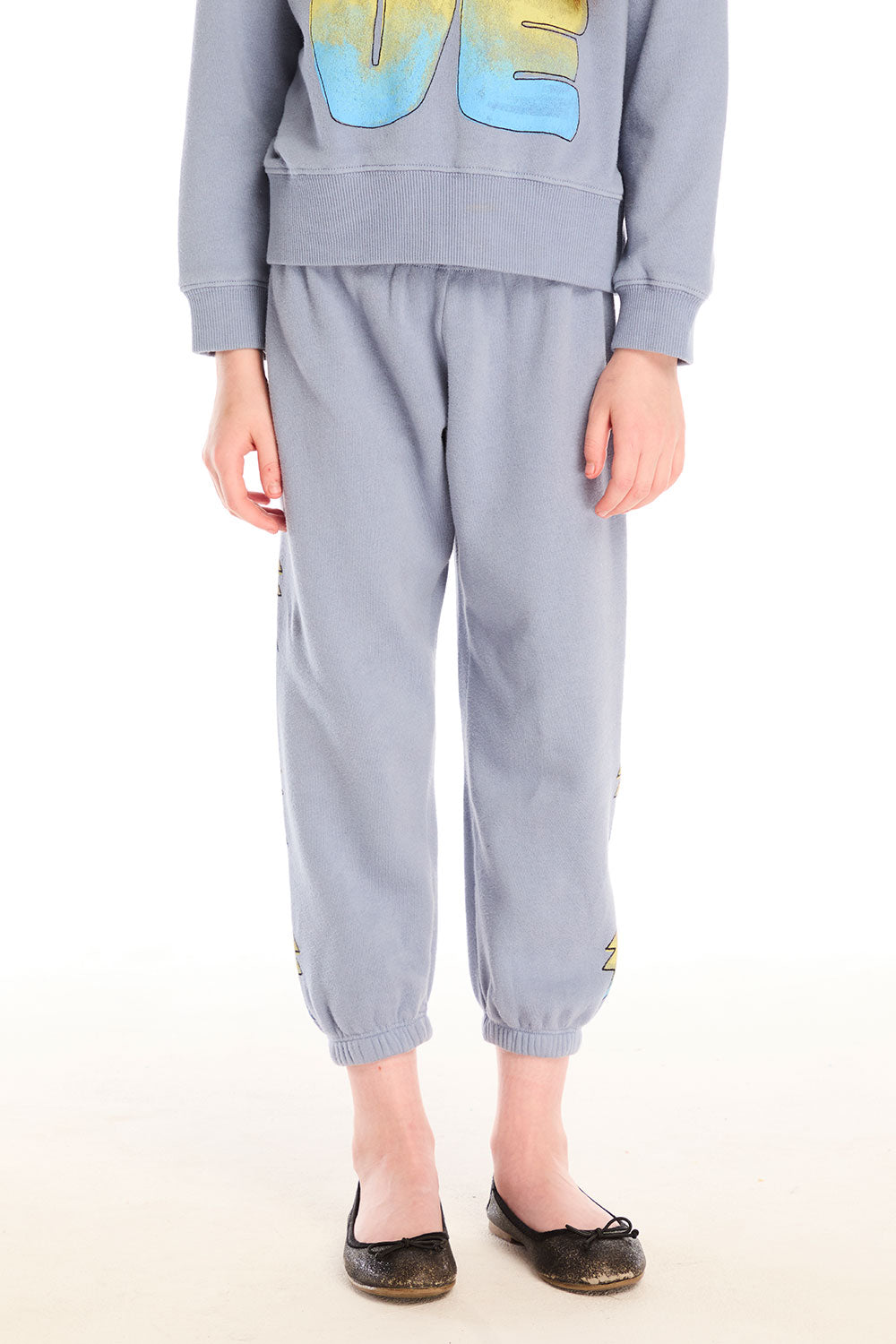 Girl wearing Chaser’s blue-gray Pastel Love Bolt Pants with colorful accents on a white background