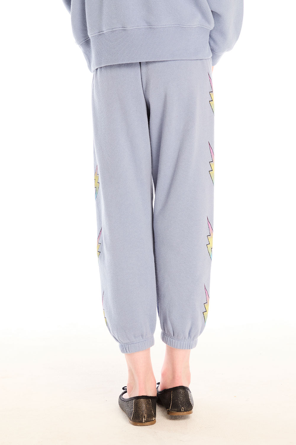 Back view of girl wearing Chaser’s blue-gray Pastel Love Bolt Pants with colorful accents on a white background