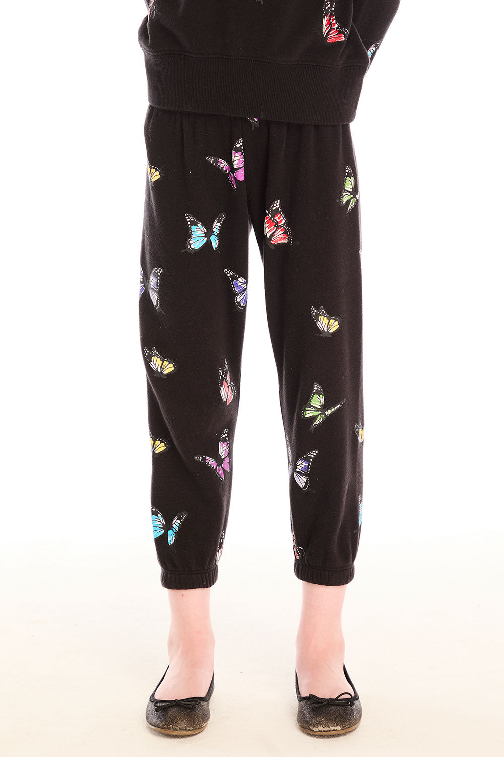 Young girl wearing Chaser’s Butterfly Love pants with colorful butterfly patterns on a white background