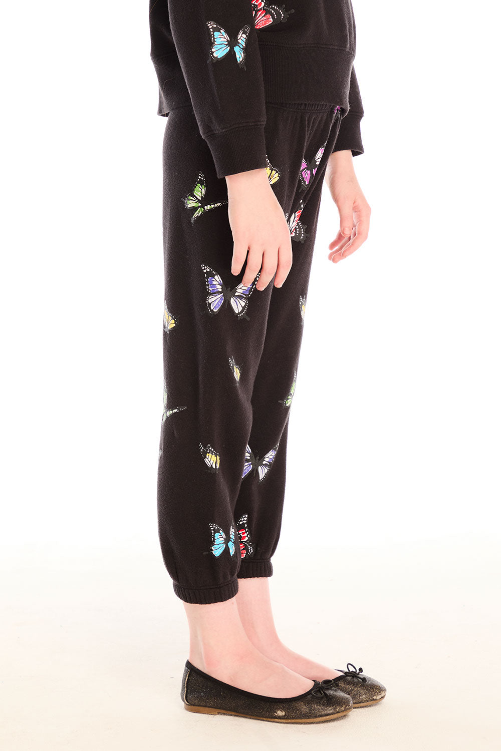 Side view of young girl wearing Chaser’s Butterfly Love pants with colorful butterfly patterns on a white background