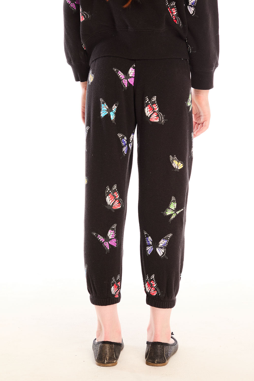 Back view of young girl wearing Chaser’s Butterfly Love pants with colorful butterfly patterns on a white background