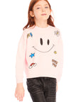 Young girl wearing Chaser’s pink Be Happy Icons long sleeve pullover with smiley face design on a white background
