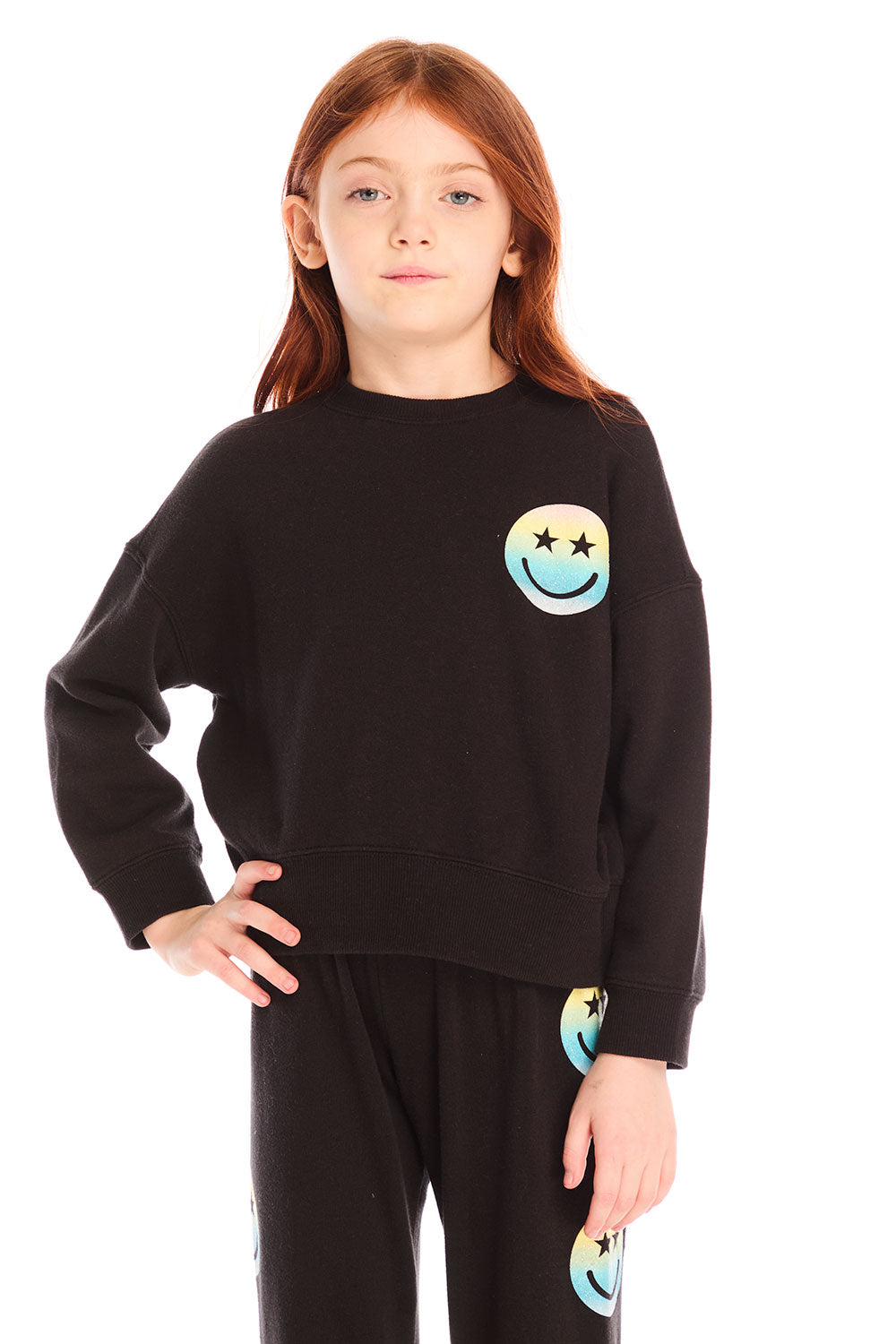Girl wearing Chaser’s black Pastel Rainbow Smiley Long Sleeve Top with pastel-colored smiley face designs on a white background
