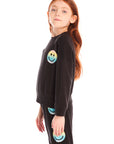 Side view of girl wearing Chaser’s black Pastel Rainbow Smiley Long Sleeve Top with pastel-colored smiley face designs on a white background