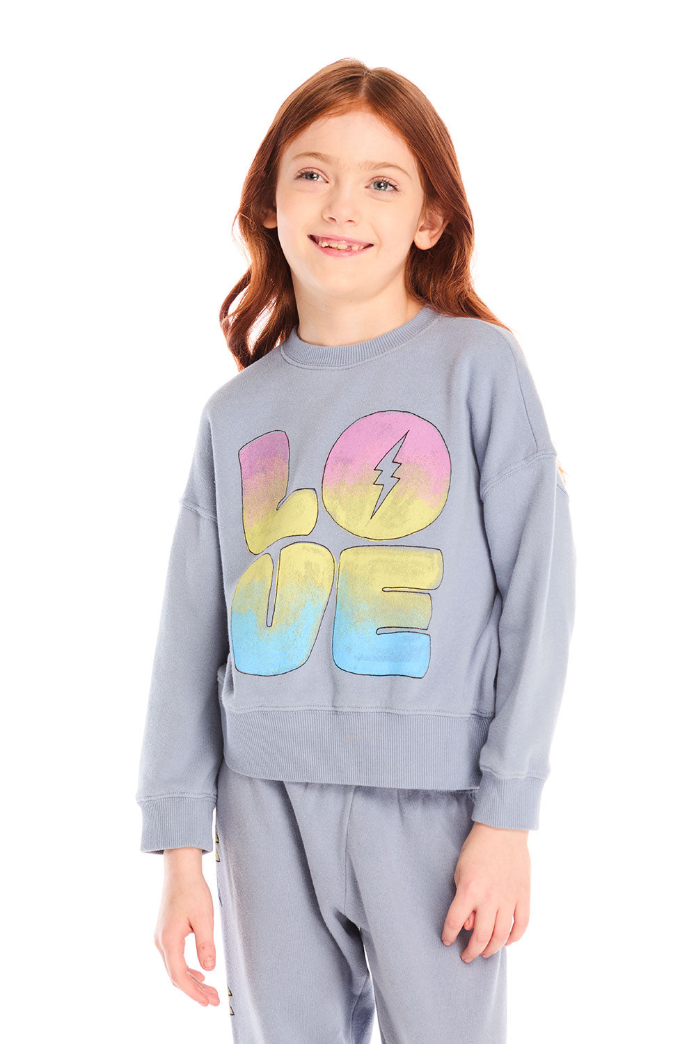 Girl wearing Chaser’s blue-gray Pastel Love Bolt Long Sleeve with colorful “LOVE” design on a white background