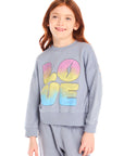 Girl wearing Chaser’s blue-gray Pastel Love Bolt Long Sleeve with colorful “LOVE” design on a white background