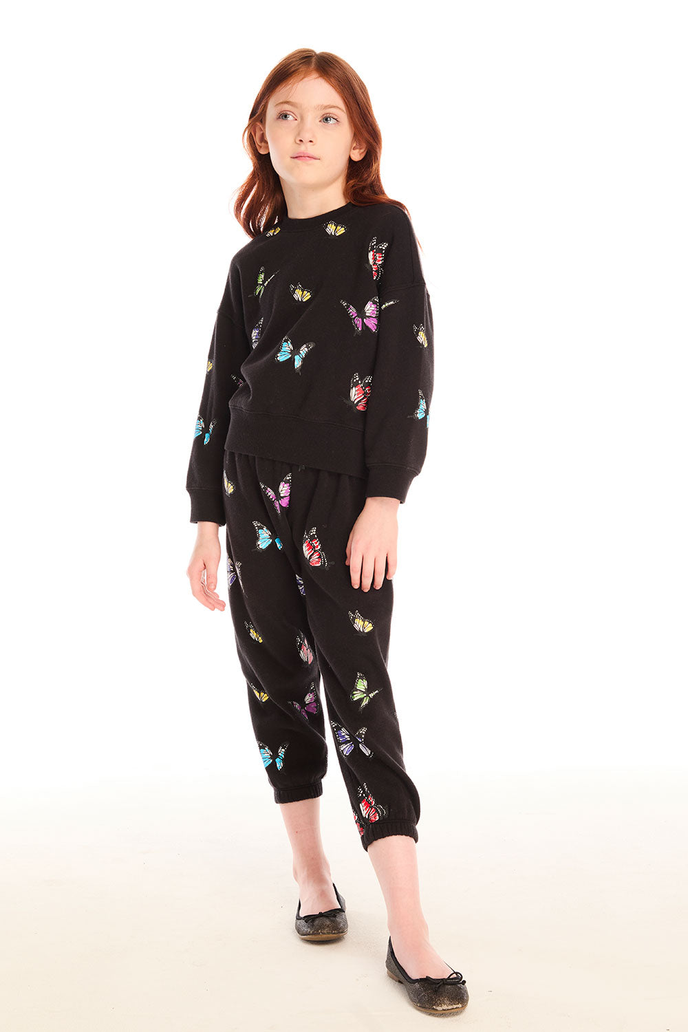 Full body view of young girl wearing Chaser’s Butterfly Love black long sleeve pullover with colorful butterfly patterns and matching pants on a white background
