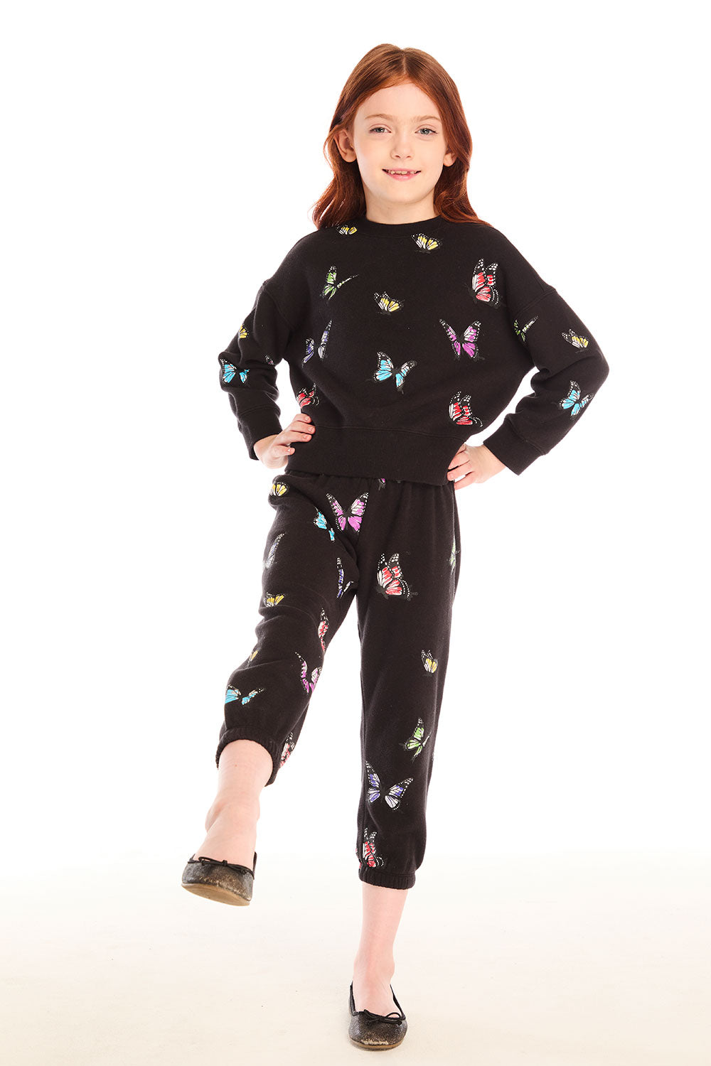 Full body view of young girl wearing Chaser’s Butterfly Love pants with colorful butterfly patterns and matching black pullover top on a white background