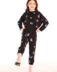 Full body view of young girl wearing Chaser’s Butterfly Love pants with colorful butterfly patterns and matching black pullover top on a white background