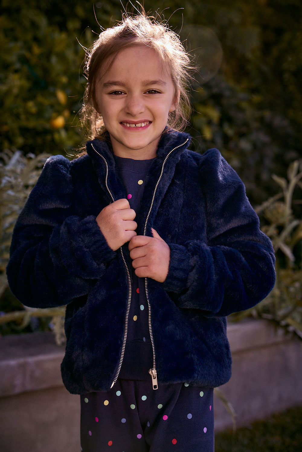 Chaser Kids Avalon Girls Puff-Sleeve Jacket in navy plush fabric with a front zipper, front view outdoors beside a low wall and greenery