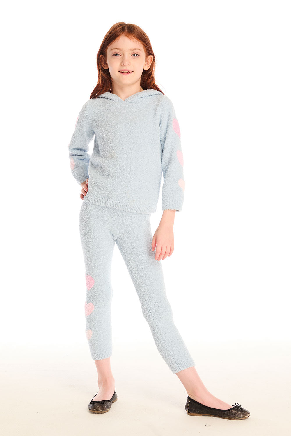 Full body view of girl wearing Chaser’s Slim Snowflake Legging pants with matching Cropped Shirred Snowflake Pullover Hoodie in light blue with pink heart sleeve accents on a white background