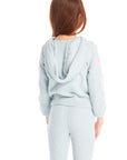 Back view of girl wearing Chaser’s Cropped Shirred Snowflake Pullover Hoodie in light blue with pink heart sleeve accents and matching Slim Snowflake Legging pants on a white background 
