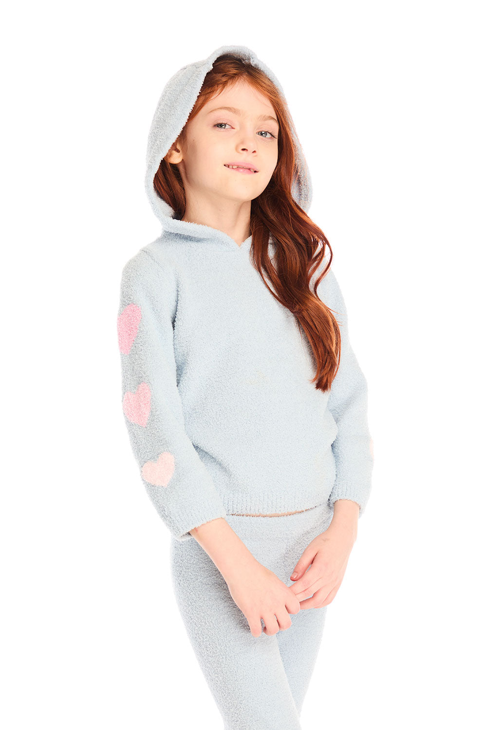 Girl wearing Chaser's light blue Cropped Shirred Snowflake Pullover Hoodie, hood up, with pink hearts on the sleeves on a white background