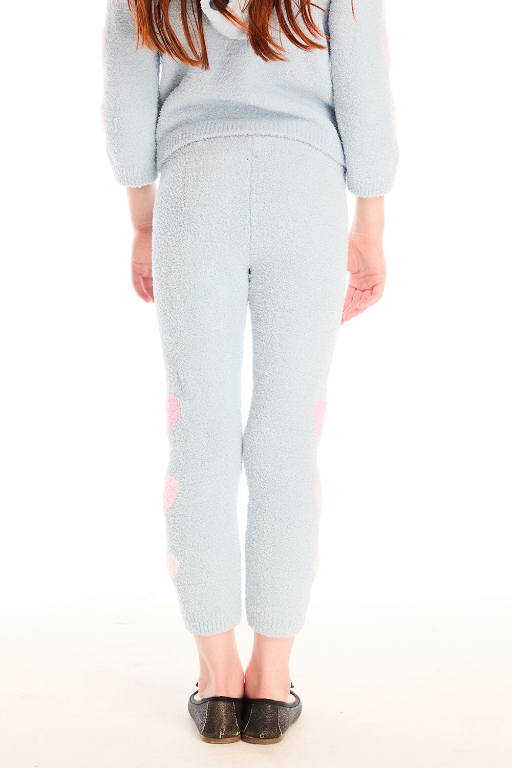 Back view of girl wearing Chaser’s Slim Snowflake Legging pants with pink hearts on legs and matching Cropped Shirred Snowflake Pullover Hoodie in light blue with pink heart sleeve accents on a white background