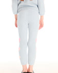 Back view of girl wearing Chaser’s Slim Snowflake Legging pants with pink hearts on legs and matching Cropped Shirred Snowflake Pullover Hoodie in light blue with pink heart sleeve accents on a white background
