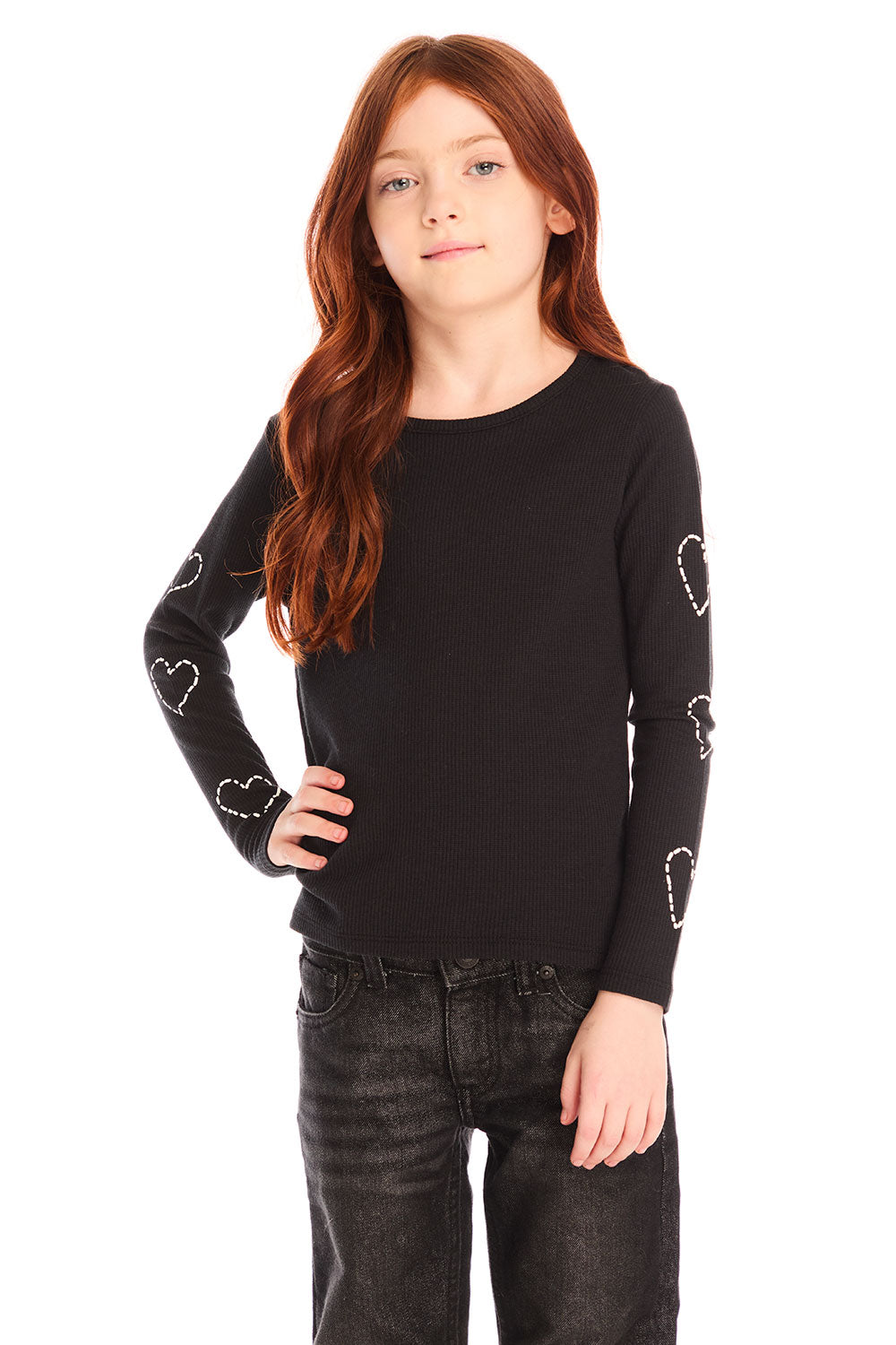 Girl wearing Chaser’s black Love Stitch Hearts Long Sleeve with heart patterns on sleeves and dark jeans on a white background