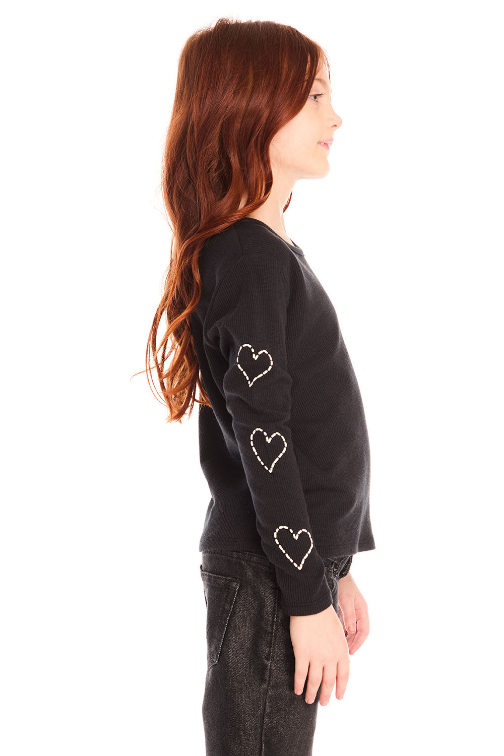 Side view of girl wearing Chaser’s black Love Stitch Hearts Long Sleeve with heart patterns on sleeves on a white background