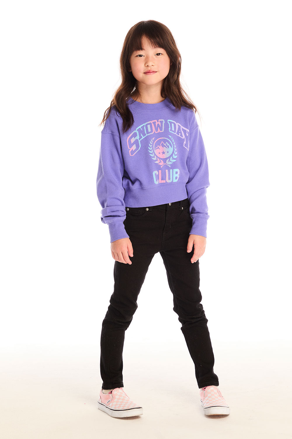 Full body view of girl wearing Chaser’s purple Snow Day Athletic Club long sleeve with text and graphics and black jeans on a white background