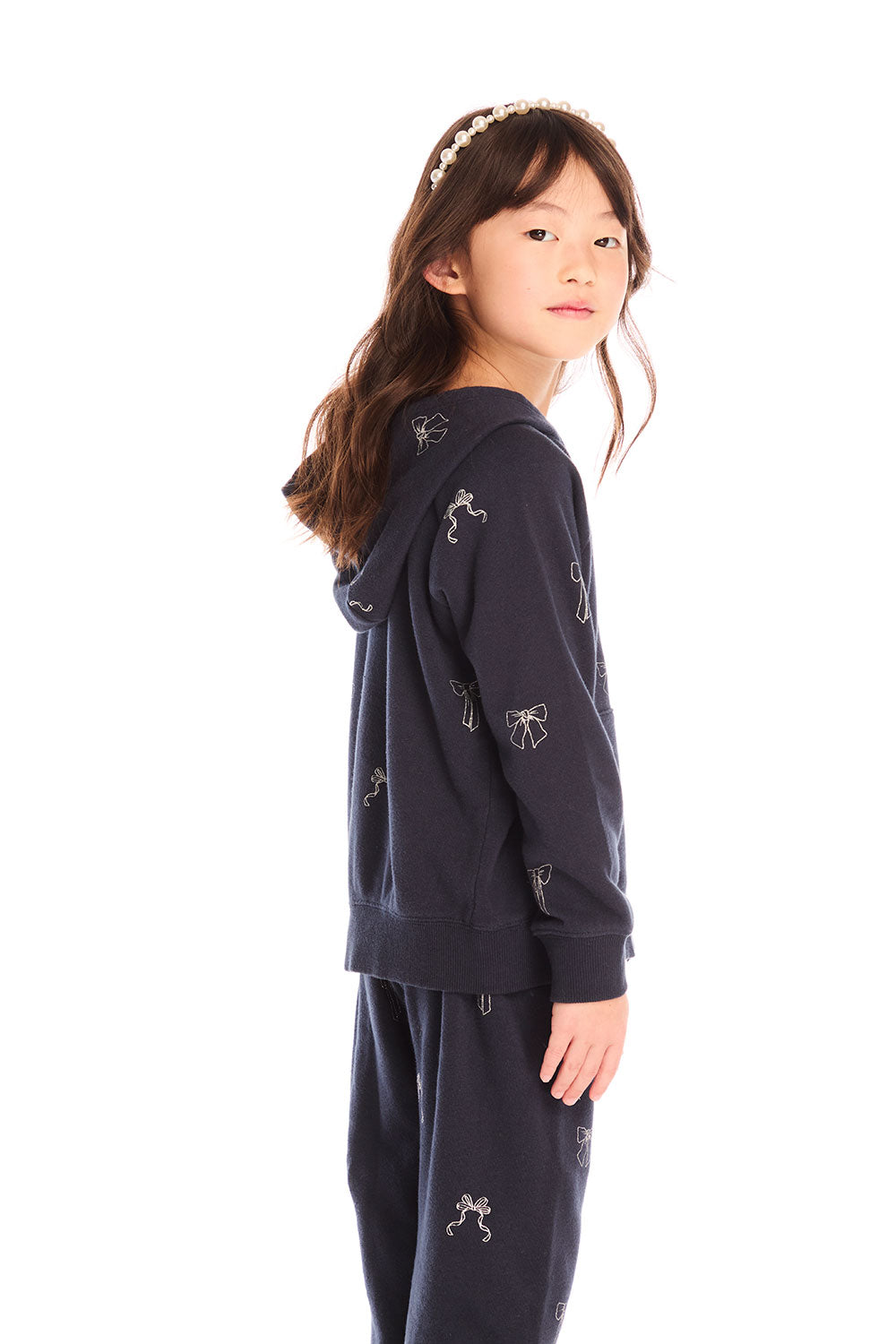 Side view of girl wearing Chaser’s navy blue Tossed Glitter Bows Zip Up Hoodie with embroidered bows on a white background