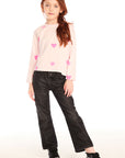 Full body view of young girl wearing Chaser’s Allover Hearts light pink pullover with heart patterns and black jeans on a white background