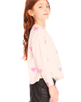 Side view of young girl wearing Chaser’s Allover Hearts light pink pullover with heart patterns on a white background