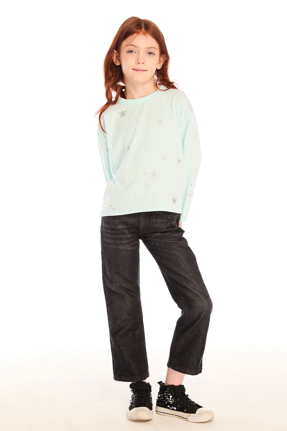 Full body view of young girl wearing Chaser’s Ciao Allover Stars light green pullover with light grey star patterns and dark jeans on a white background