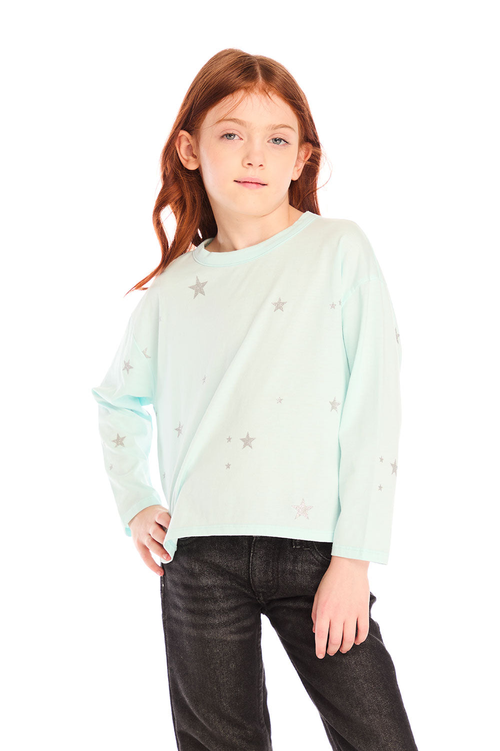 Young girl wearing Chaser’s Ciao Allover Stars light green pullover with light grey star patterns and dark jeans on a white background