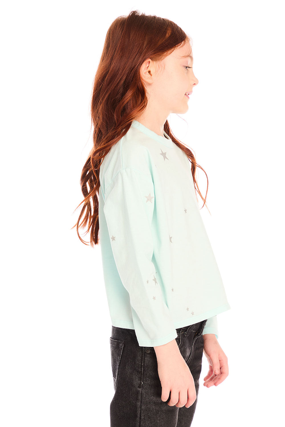 Side view of young girl wearing Chaser’s Ciao Allover Stars light green pullover with light grey star patterns and dark jeans on a white background
