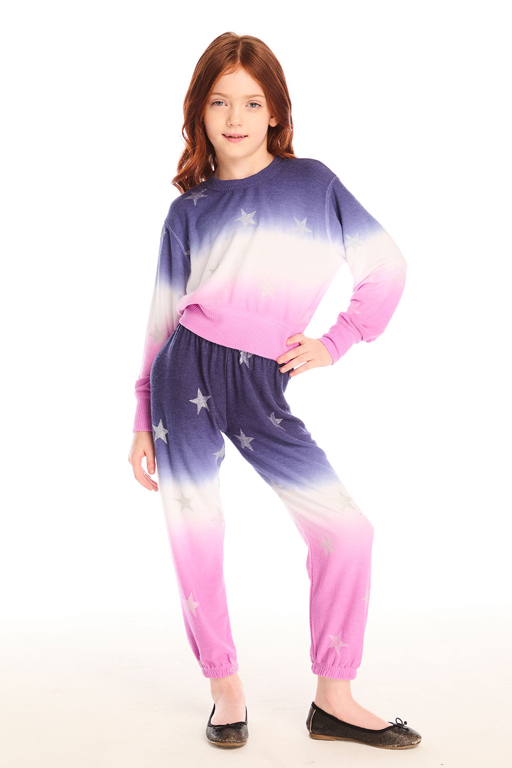 Full body view of girl wearing Chaser’s Slim Ombre Tie Dye Pants with colorful glitter star patterns and matching long sleeve top on a white background