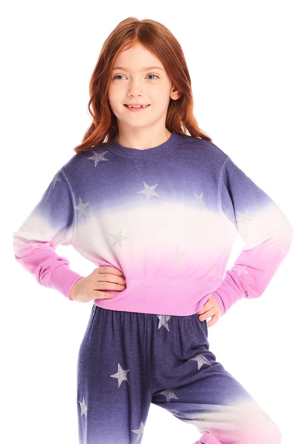 Girl wearing Chaser’s Glitter Stars Ombre Tie Dye Long Sleeve with colorful star patterns and matching pants on a white background