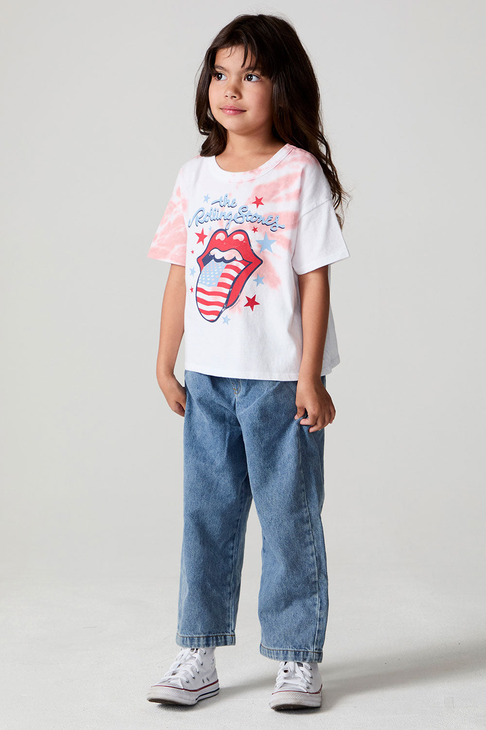 A full body side angle view of a girl wearing the Chaser The Rolling Stones Americana Stones Tee and jeans on a neutral background
