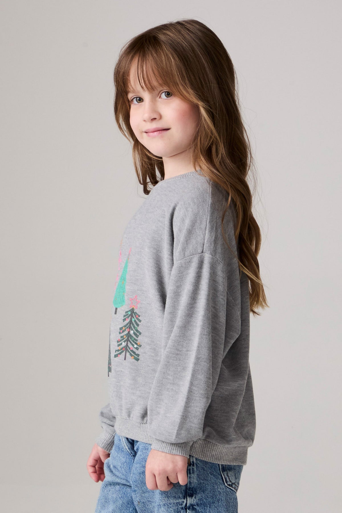 Model wearing Chaser's Festive Trees Girls Pullover in heather grey with distinctive graphic and design details, side view