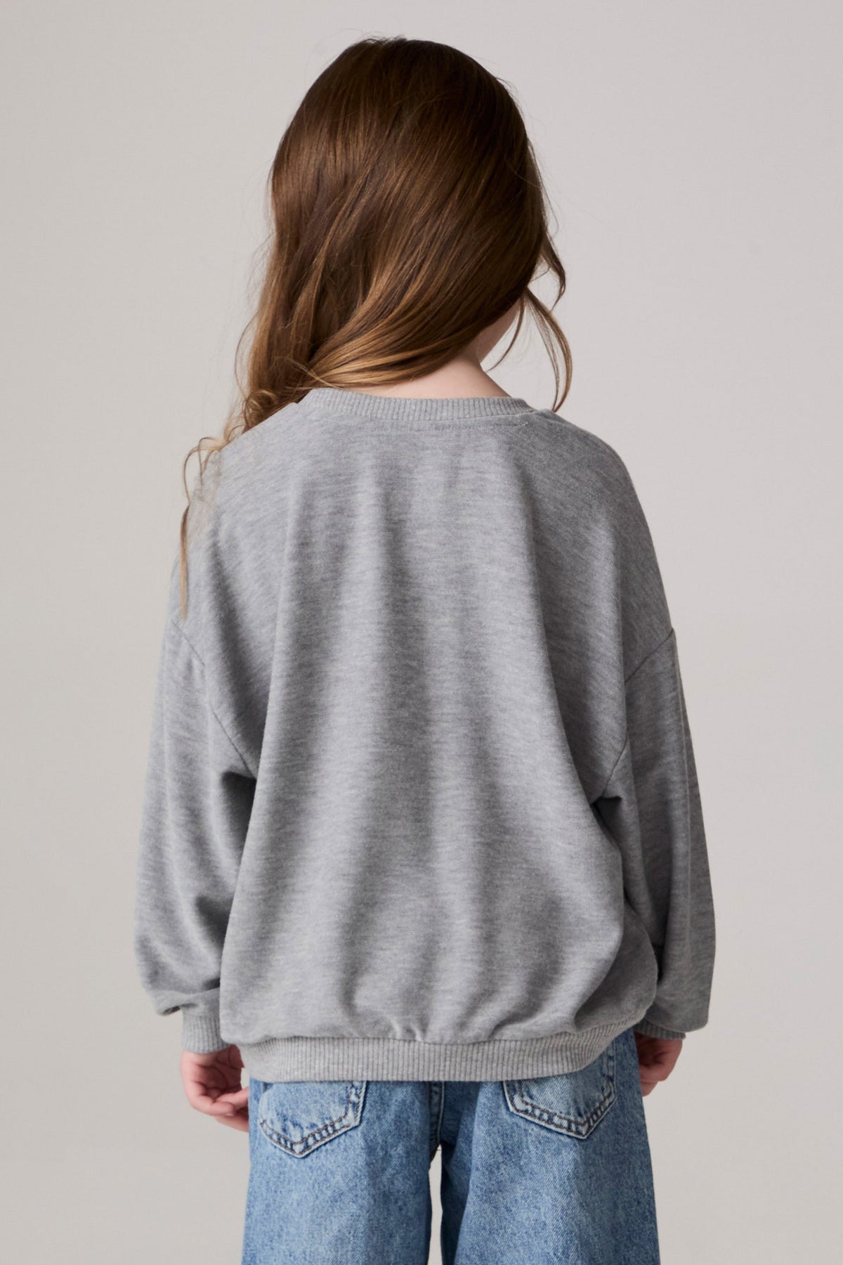 Model wearing Chaser's Festive Trees Girls Pullover in heather grey with distinctive graphic and design details, back view