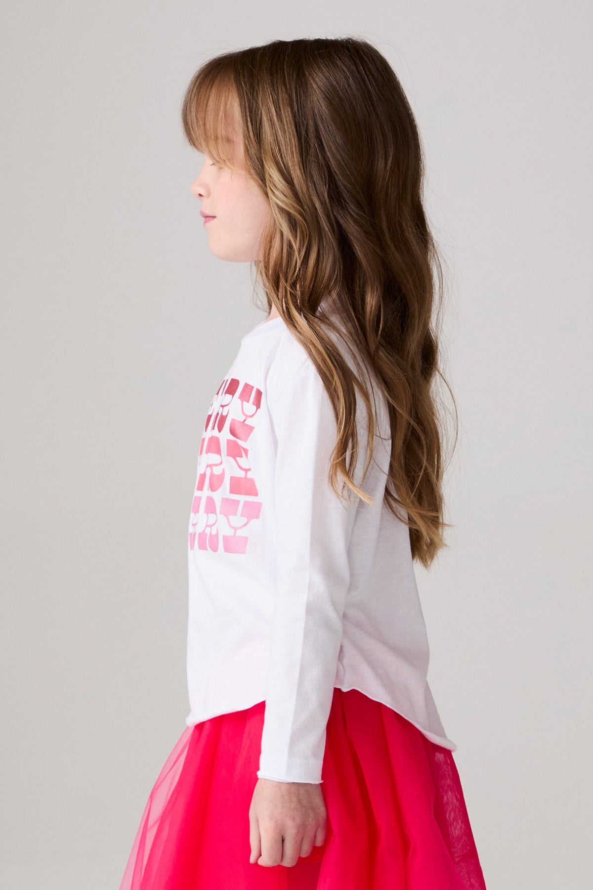 Model wearing Chaser's Merry Girls Long Sleeve Tee in white with pink and red Merry lettering, side view