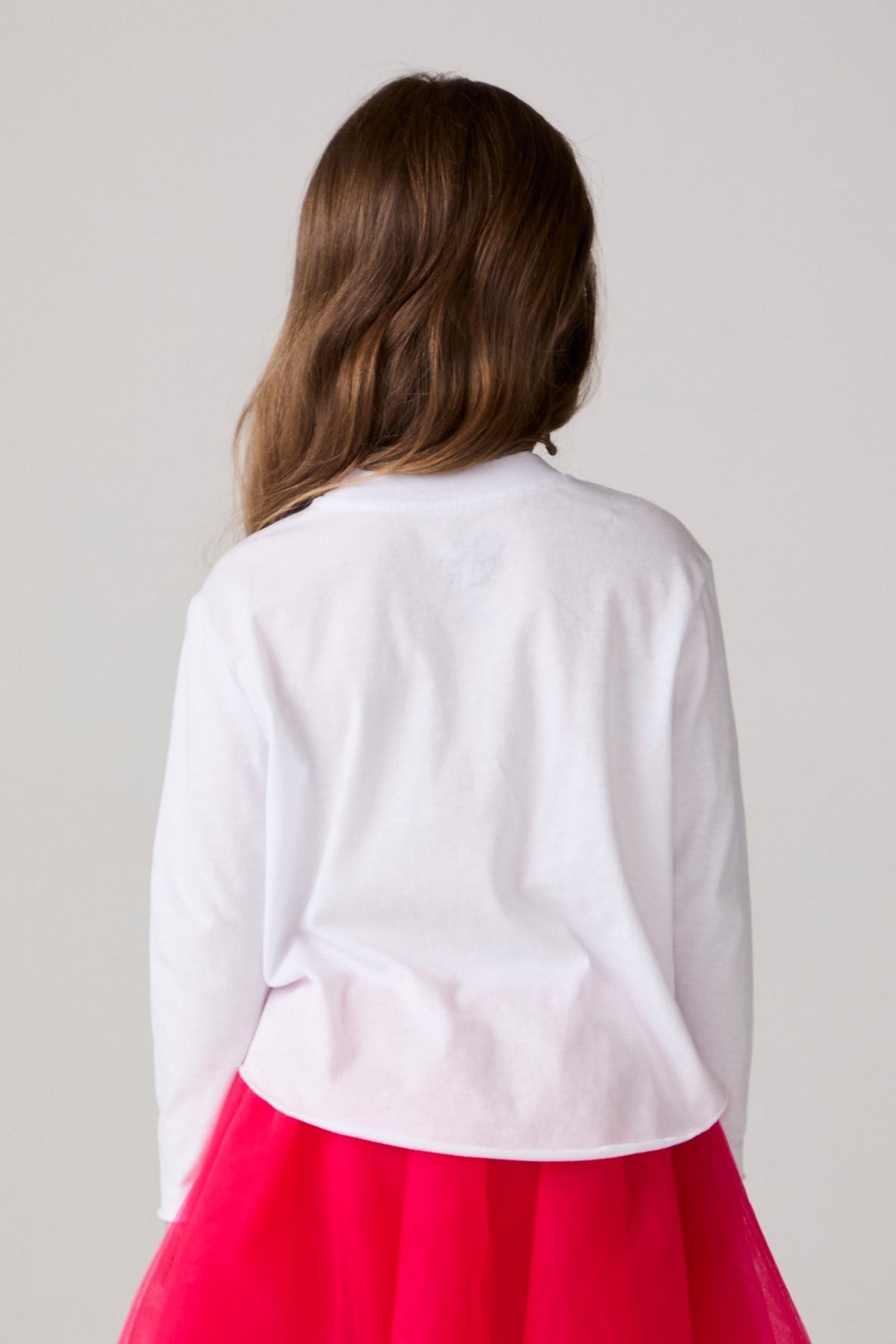 Model wearing Chaser's Merry Girls Long Sleeve Tee in white with pink and red Merry lettering, back view