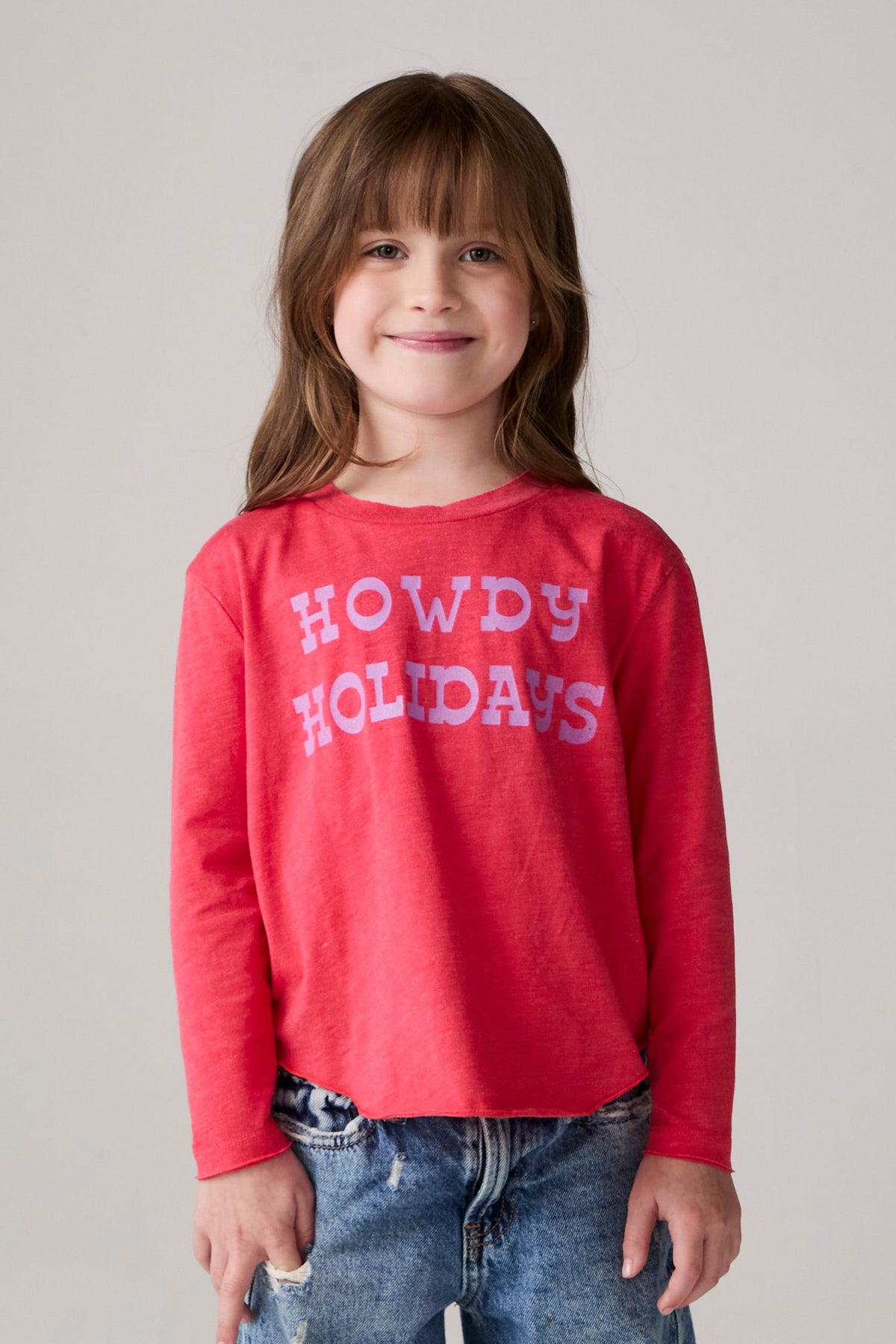 Model wearing Chaser's Howdy Holidays Girls Long Sleeve Tee in hibiscus with western holiday graphic, front view
