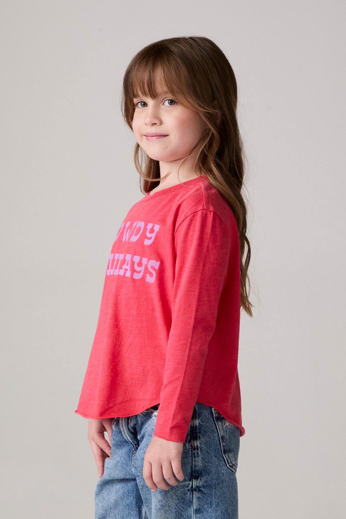 Model wearing Chaser's Howdy Holidays Girls Long Sleeve Tee in hibiscus with western holiday graphic, side view