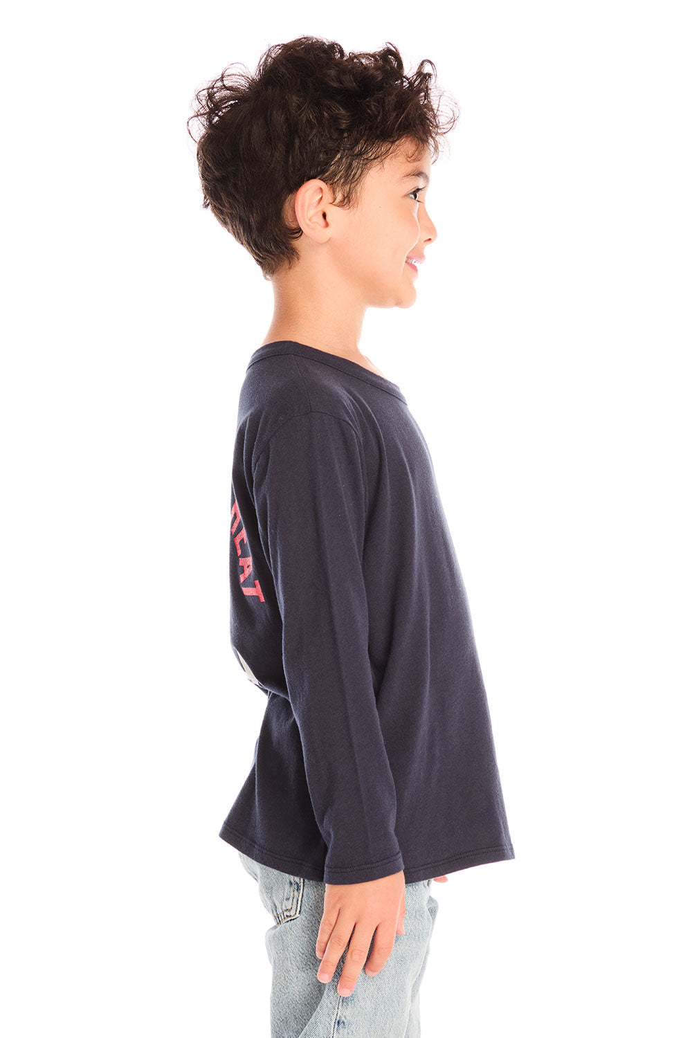 Side view of boy wearing Chaser’s Bring The Heat black long-sleeve shirt with logo, light blue jeans, and brown boots on a white background.