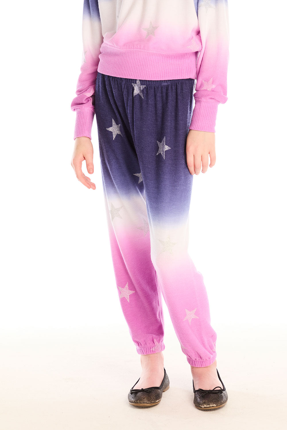 Girl wearing Chaser’s Slim Ombre Tie Dye Pants with colorful glitter star patterns and matching long sleeve top on a white background