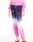 Girl wearing Chaser’s Slim Ombre Tie Dye Pants with colorful glitter star patterns and matching long sleeve top on a white background