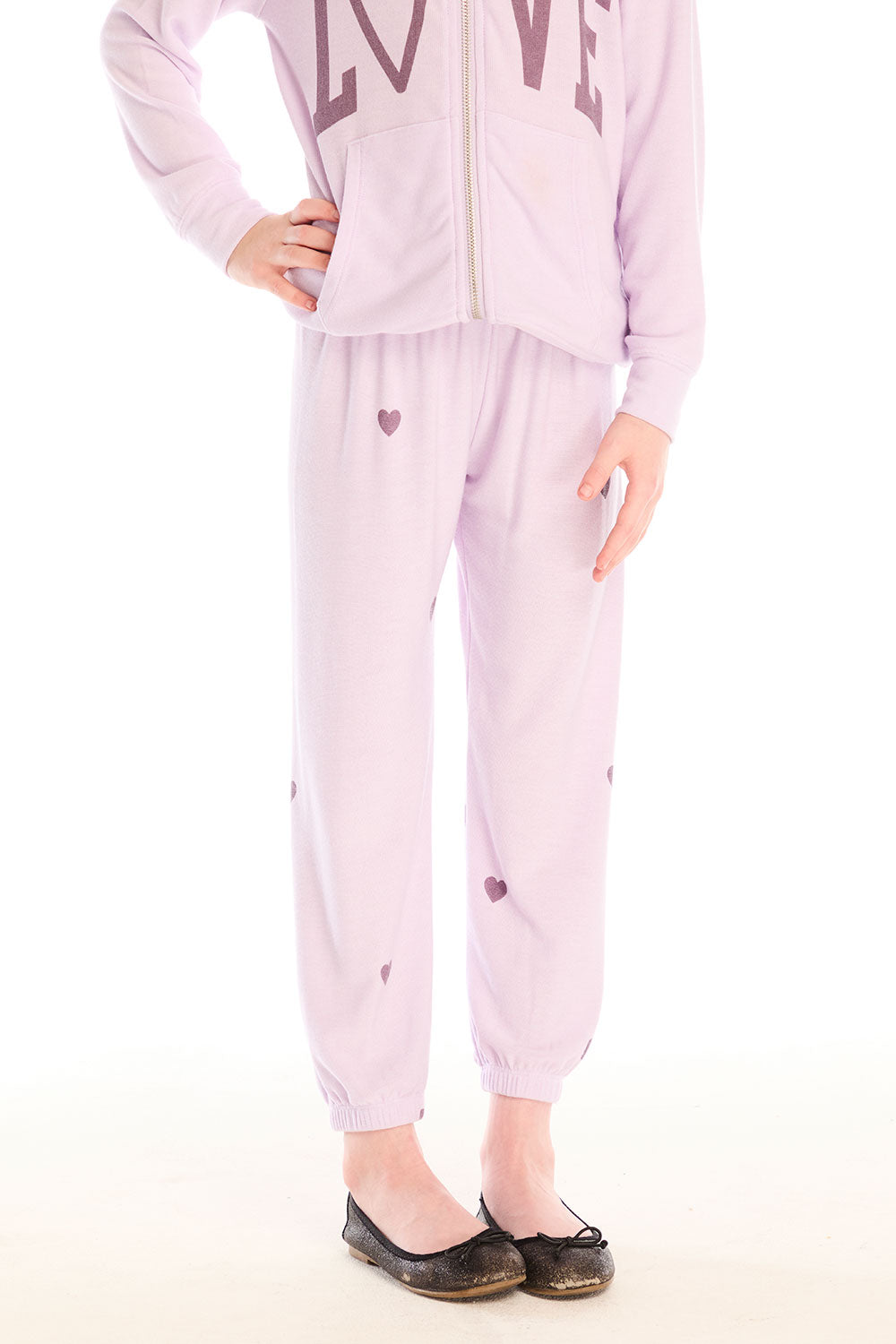 Girl wearing Chaser’s pink Love Pants with heart prints on a white background